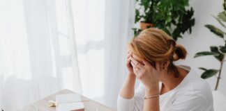 A woman sitting at a desk with her hands on her face, surrounded by paperwork and money, looking stressed