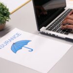 SHOCKING Insurance Ripoff Exposed Nationwide A person typing on a laptop next to an insurance document and a small plant