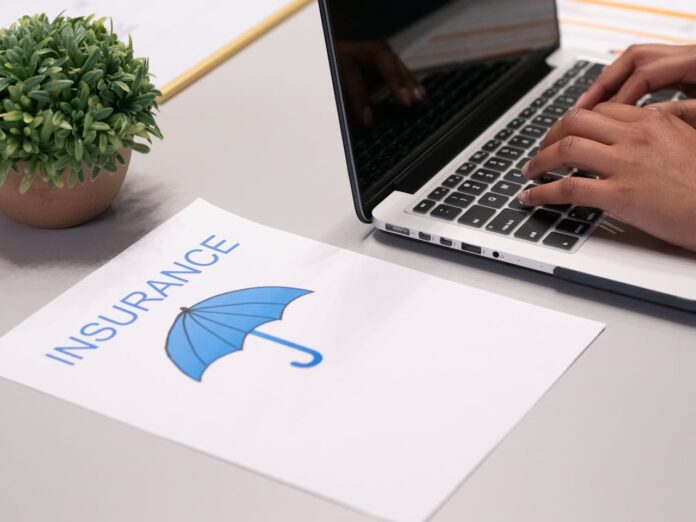 A person typing on a laptop next to an insurance document and a small plant