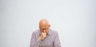 An older man reading a newspaper while sitting at a wooden table with a coffee cup
