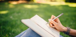 Person writing in a notebook while sitting on grass