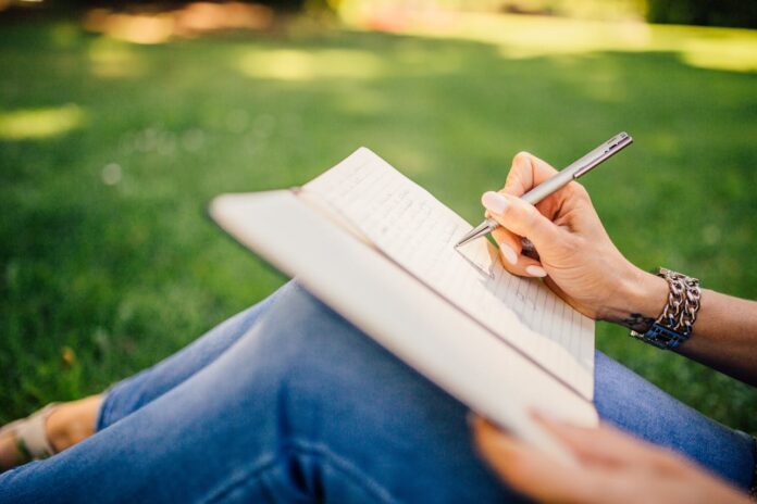Person writing in a notebook while sitting on grass