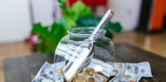 A glass jar filled with coins and a scoop, surrounded by dollar bills