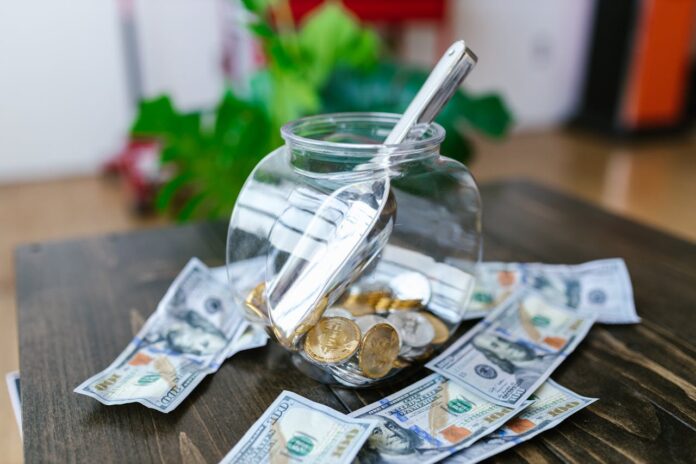 A glass jar filled with coins and a scoop, surrounded by dollar bills