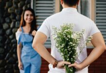 A man hiding a bouquet of flowers behind his back while smiling at a woman